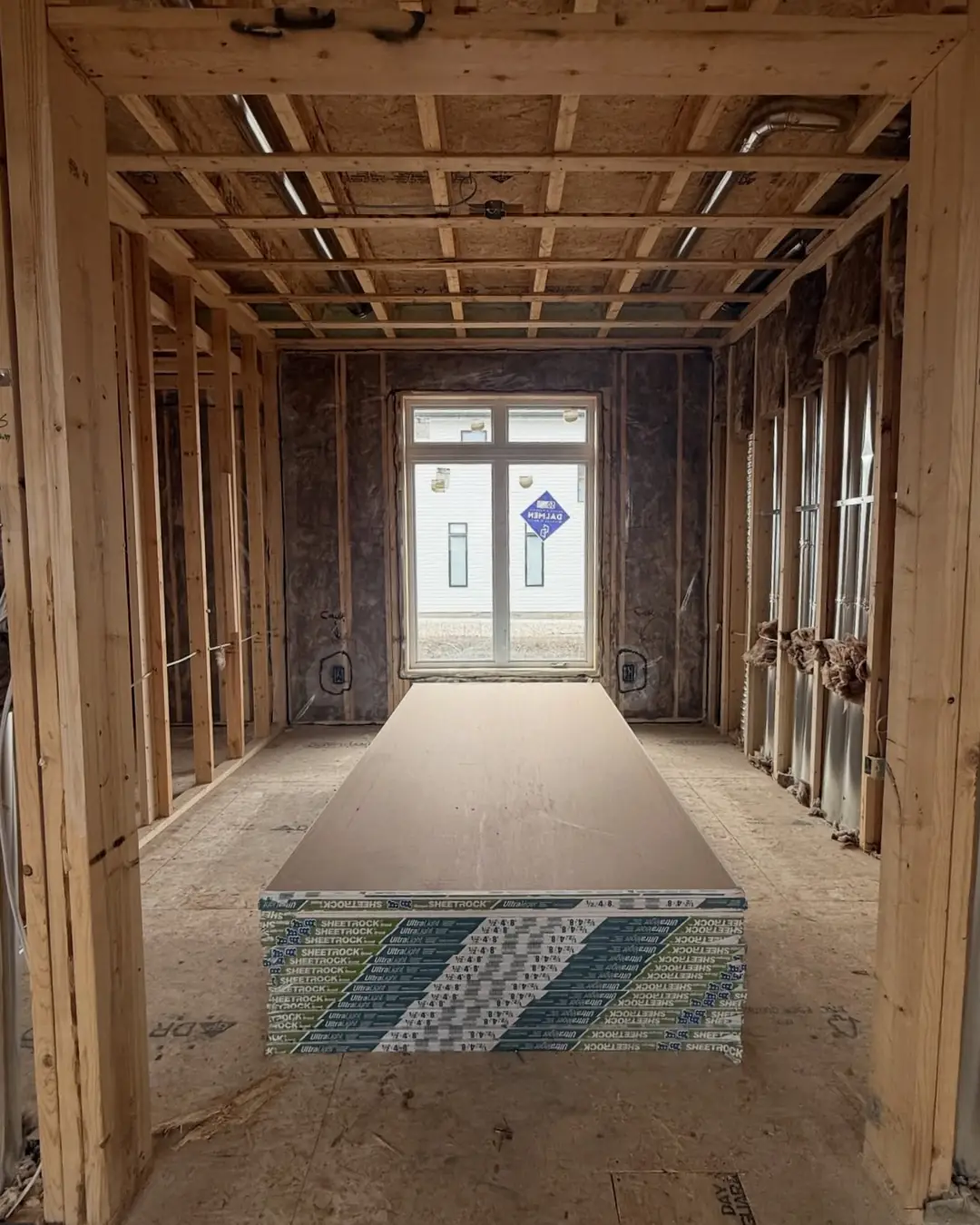 Before: a framed and insulated room in Findlay Creek with a stack of drywall in the middle of the floor.