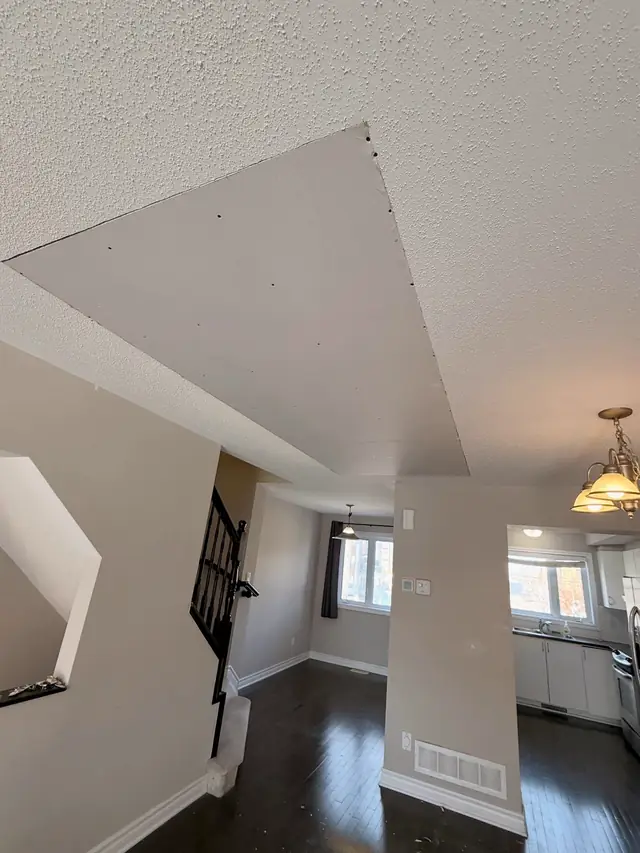 A new drywall patch on a ceiling in a lived-in Barrhaven home, above hardwood floors and the kitchen.