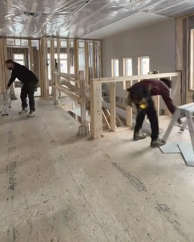 Two of the KOSO crew hanging drywall at the top of a stairway in a new house, faces turned away.