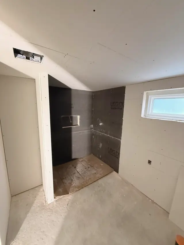 A basement storage room turned into a laundry and washroom: walls boarded, the shower in backer board, a small window.