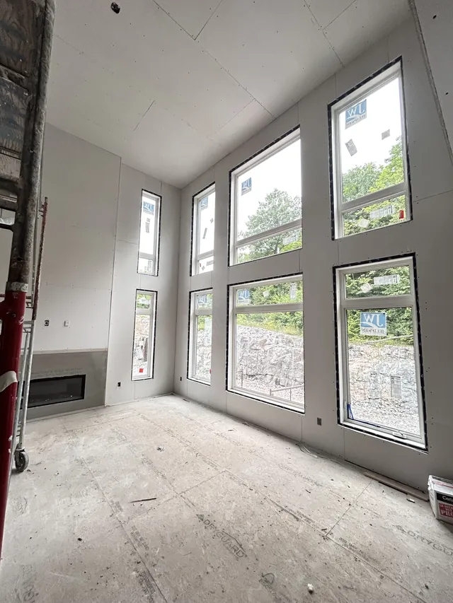 A tall great room wall of windows with the drywall hung around every frame, the floor still bare.